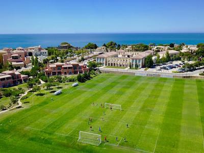 Großes Fußballfeld neben Hotelgebäuden mit Blick auf das Meer bei klarem Himmel.