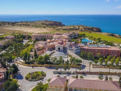 Luftaufnahme einer Küstenstadt mit Gebäuden, Straßen, Grünflächen und blauem Meer im Hintergrund.
