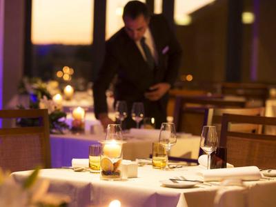 Elegantes Restaurant mit gedecktem Tisch, Kerzenlicht und einem Gast im Hintergrund bei Dämmerung.