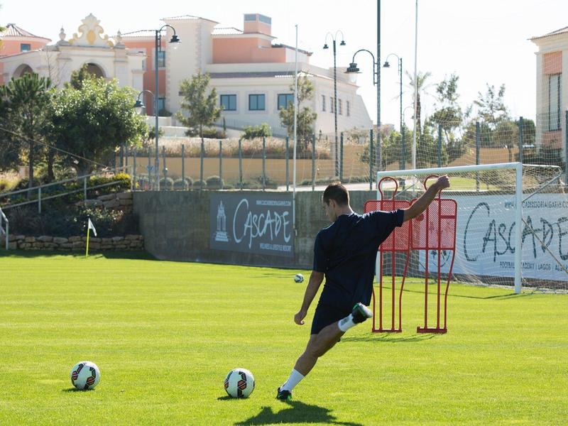 Ein Mann schießt auf einem Fußballfeld mit mehreren Bällen und Trainingsausrüstung.
