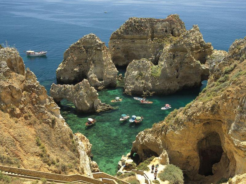 Felsige Küste mit türkisfarbenem Wasser und kleinen Booten zwischen hohen Klippen.