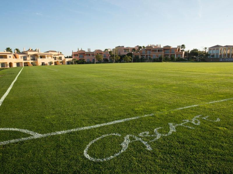 Freiluft-Tennisplatz mit blauem Spielfeld und grünem Umfeld unter klarem Himmel.