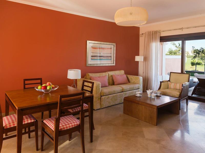 Helles Wohnzimmer mit Terrakottawand, Esstisch, Sofa, Sesseln und Zugang zum Balkon mit Grünblick.