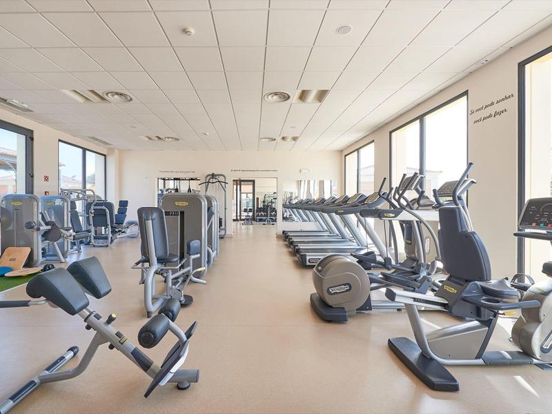 Heller, moderner Fitnessraum mit zahlreichen Laufbändern, Ergometern und Kraftgeräten an großen Fenstern.