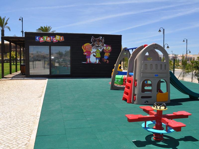 Kinderspielplatz mit Rutsche, Wippe, Klettergerüst und Gebäude mit bunter Wandgestaltung.