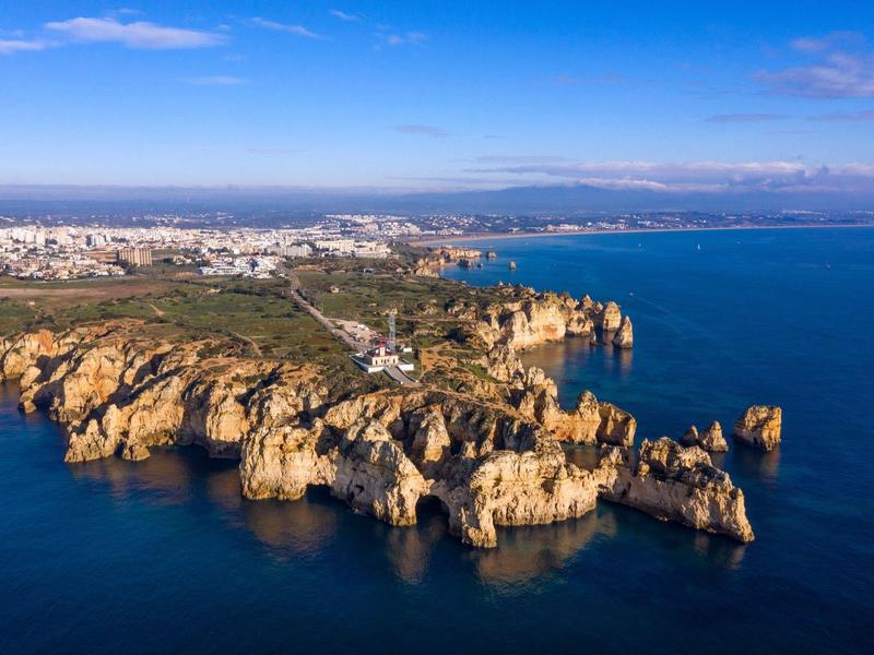 Küste mit markanten Felsformationen, blauem Meer und Stadt am Horizont unter klarem Himmel.