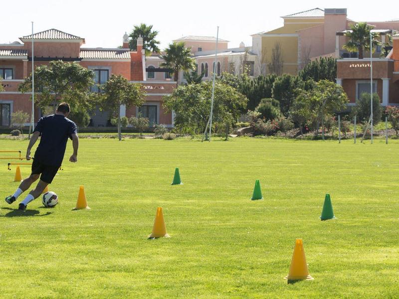 Person trainiert Fußball mit Ball auf grünem Rasen zwischen orange-grünen Hütchen.
