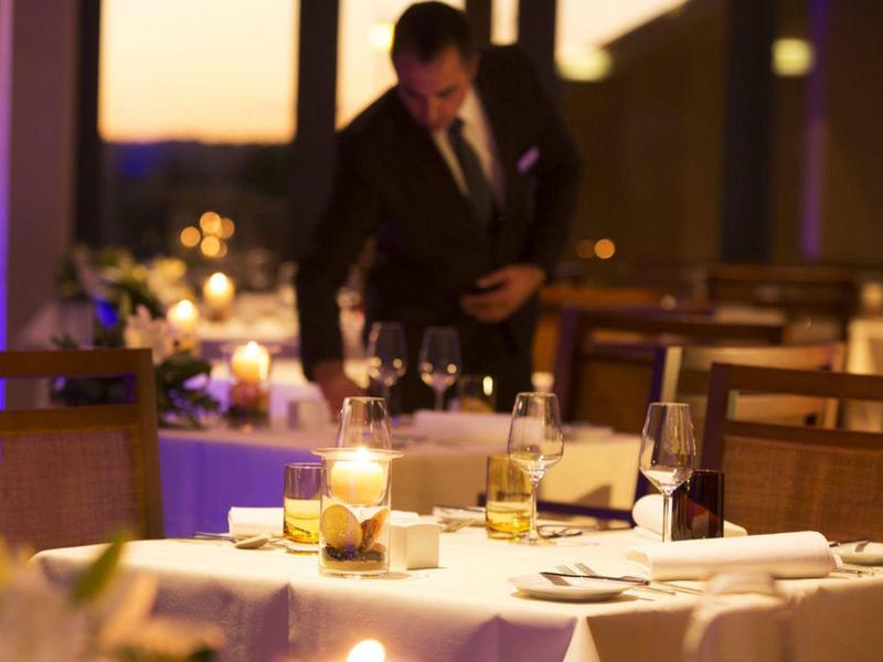 Elegantes Restaurant mit gedecktem Tisch, Kerzenlicht und einem Gast im Hintergrund bei Dämmerung.