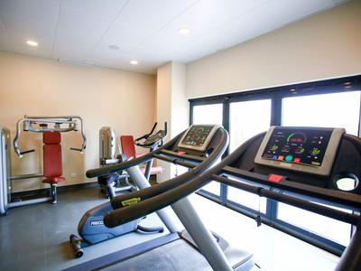 Moderner Fitnessraum mit Laufbändern und Krafttrainingsgeräten vor großen Fenstern