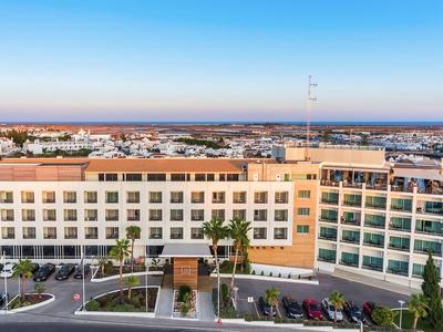 Großes modernes Bürogebäude mit Parkplätzen und klar blauem Himmel im Hintergrund.