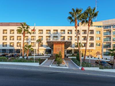 Großes, fünfstöckiges Gebäude mit beige-farbenem Fassadenfront und Palmen im Eingangsbereich.