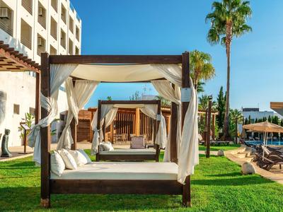 Luxuriöse Außensicht mit Holzbetten, weißen Vorhängen, grüner Wiese und blauem Himmel.