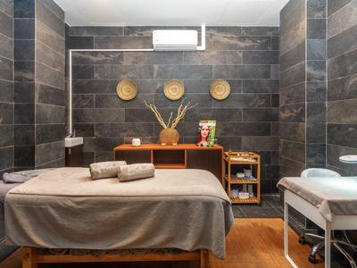 Ruhiger Wellnessraum mit zwei Massageliegen, dunklen Fliesenwänden und Holzregal mit Deko.