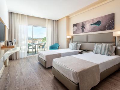 Modernes Hotelzimmer mit zwei Einzelbetten, Balkon, Flachbildfernseher und hellem Holzboden.