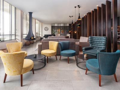 Moderne Lounge mit bunten Sesseln, großem Fenster, Kamin und Holzwand als Raumteiler.