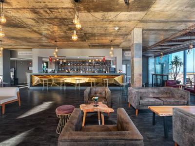 Moderner Barbereich mit Holztheke, hängenden Glühbirnen und gemütlichen Samtsofas in warmem Licht.