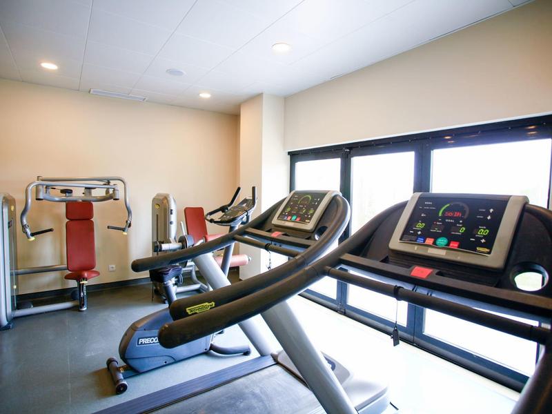 Hell beleuchteter Fitnessraum mit Laufbändern, Kraftstation und großen Fenstern.