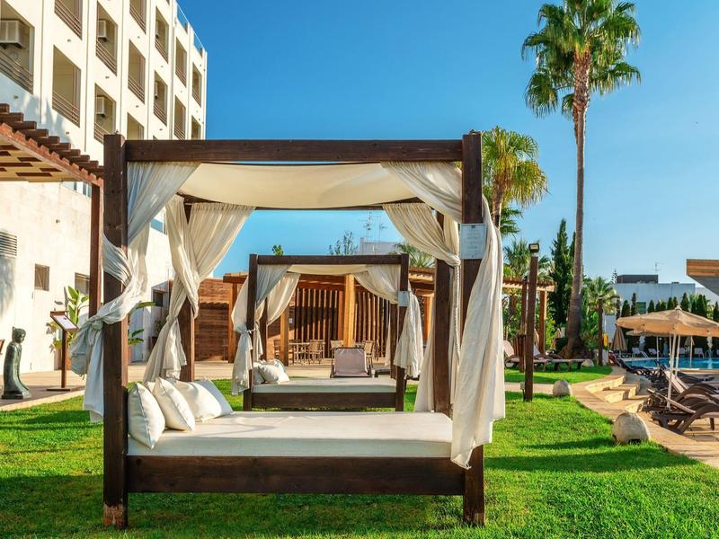 Luxuriöse Außensicht mit Holzbetten, weißen Vorhängen, grüner Wiese und blauem Himmel.