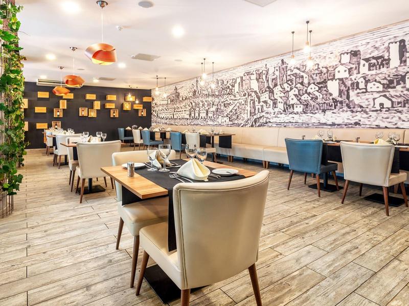 Modernes Restaurant mit hellen Holzböden, beigen Sesseln und großem Wandbild in Schwarz-Weiß.