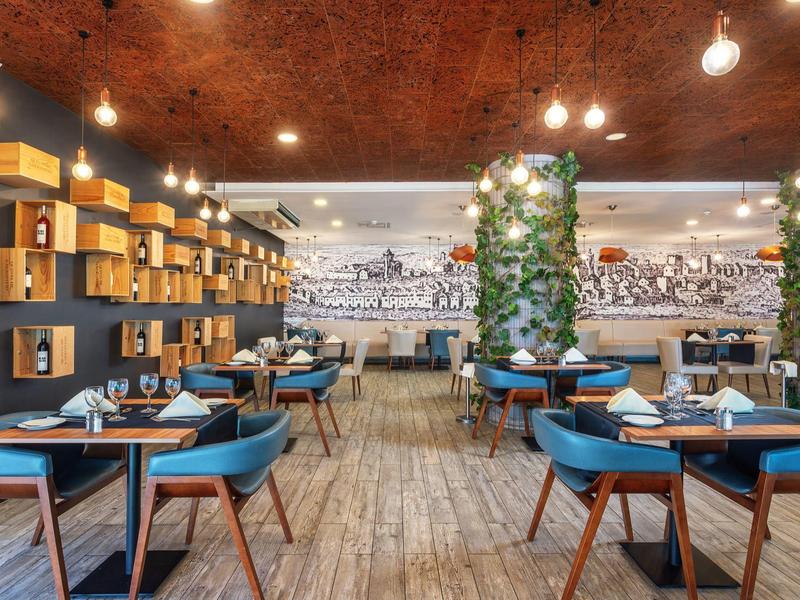 Modernes Restaurant mit blauen Stühlen, Holztischen und grüner Pflanzenwand in warmem Licht.