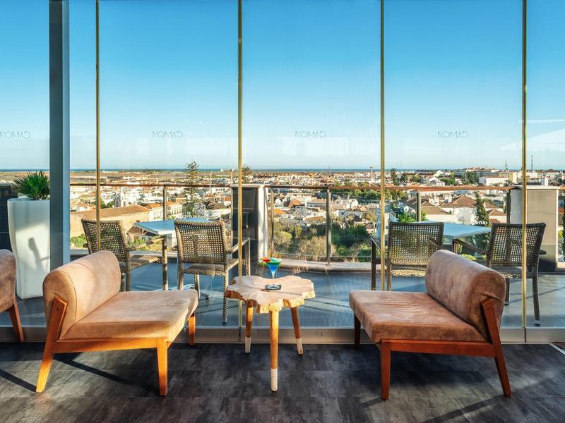 Moderne Dachterrasse mit Glasgeländer, zwei Holzbänken, kleinem Tisch und weitem Stadtblick.