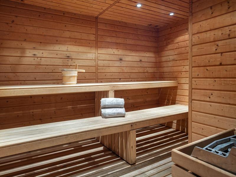 Holzsauna mit zwei Etagen, Handtüchern und Saunakübel, warmes Licht, Holzstruktur sichtbar.