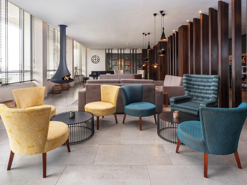 Moderne Lounge mit bunten Sesseln, großem Fenster, Kamin und Holzwand als Raumteiler.