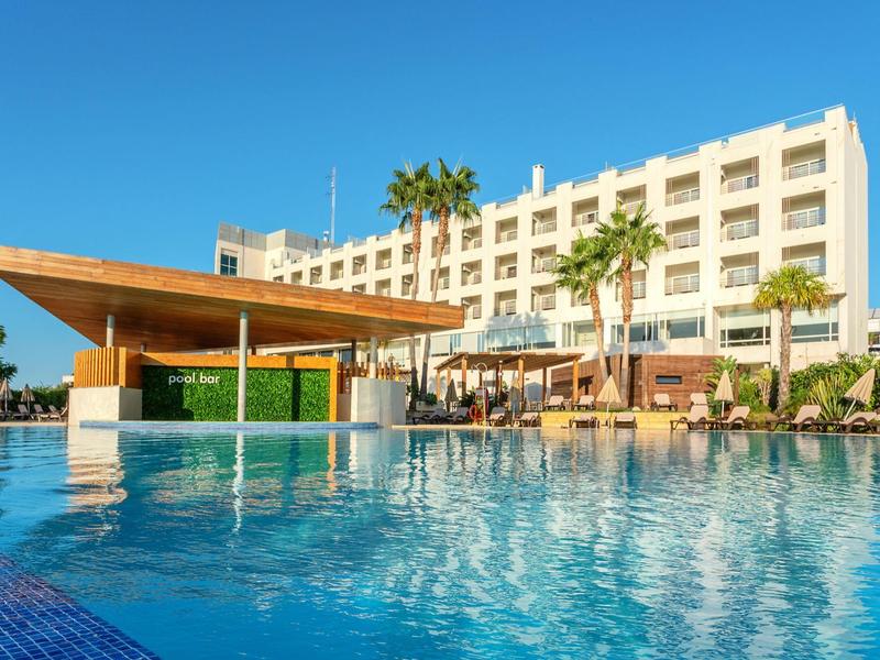 Ein großes Hotel mit Poolbar, Palmen und klarem blauem Himmel im Hintergrund.