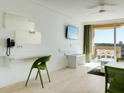 Moderner, heller Raum mit grünem Stuhl, weißem Schreibtisch, Flachbildschirm und Balkon mit Aussicht.