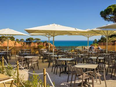 Leerer Außenbereich eines Cafés mit Tischen, Stühlen, Sonnenschirmen und Blick auf das Meer.