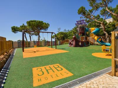 Spielplatz mit Rutschen, Sandboden und buntem Klettergerüst unter blauem Himmel.