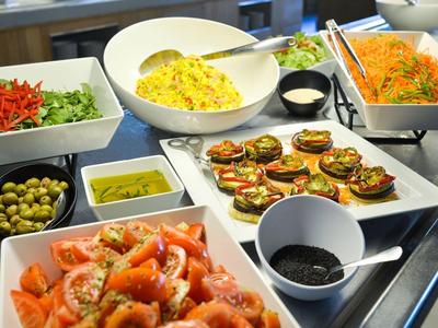 Verschiedene bunte Salate, Oliven und Dips in weißen Schalen auf einem Buffet-Tisch arrangiert.