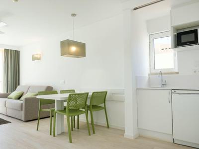 Moderner heller Wohnraum mit grauem Sofa, grünem Tisch und Stühlen, weißer Küchenzeile und Mikrowelle.