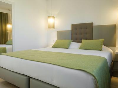 Modernes Hotelzimmer mit großem Bett und grüner Bettdecke und Kissen.