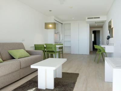 Modern eingerichtetes Wohnzimmer mit grauem Sofa, weißem Tisch und grünem Essbereich.