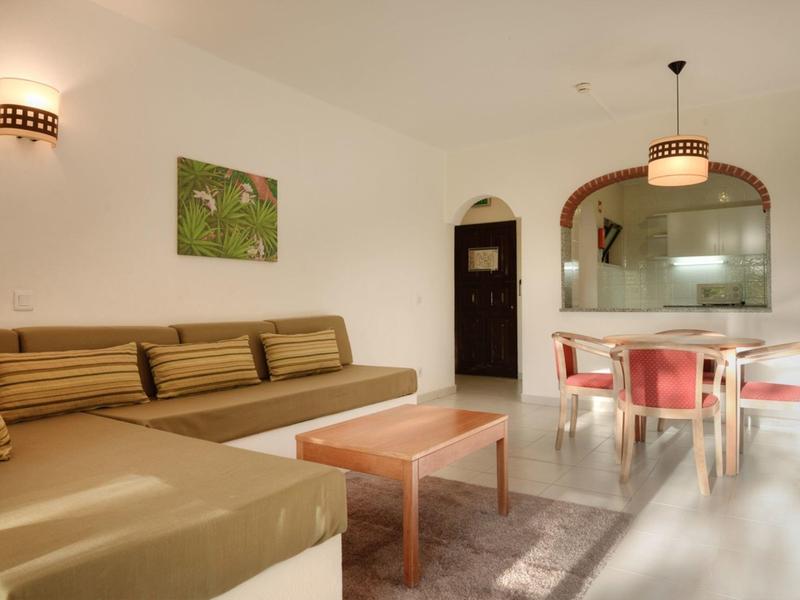 Helles Wohnzimmer mit braunem Ecksofa, Holztisch, Teppich und Esstisch mit roten Stühlen.