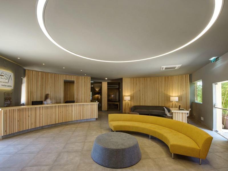 Helle Empfangshalle mit geschwungener gelber Couch, runder Lampe und Holztheke.