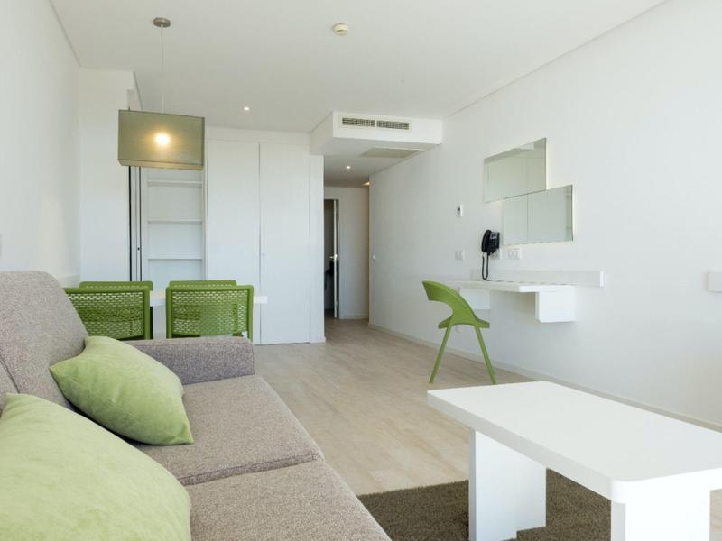 Helles Wohnzimmer mit grauem Sofa, grünen Kissen, grünem Stuhl, weißem Tisch und Holzfußboden.