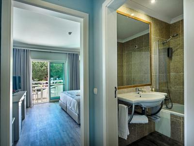 Moderner Hotelflur mit Blick auf Schlafzimmer mit Balkon und angrenzendem Badezimmer mit Wanne und Waschbecken.