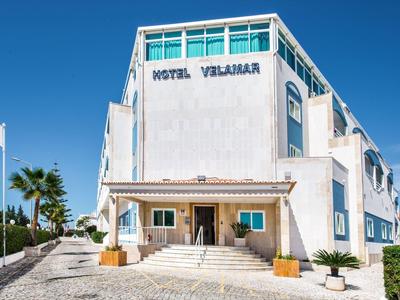 Weißes mehrstöckiges Hotelgebäude mit blauer Aufschrift "Hotel Velamara" unter klarem blauem Himmel.