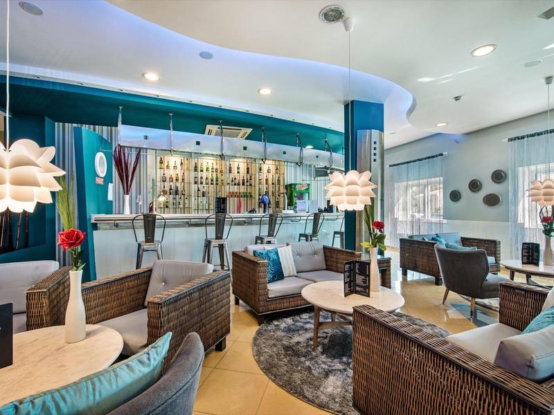 Moderner Lounge-Bereich mit Rattansesseln, runden Lampen und beleuchtetem Bar hinter Glasflaschen.