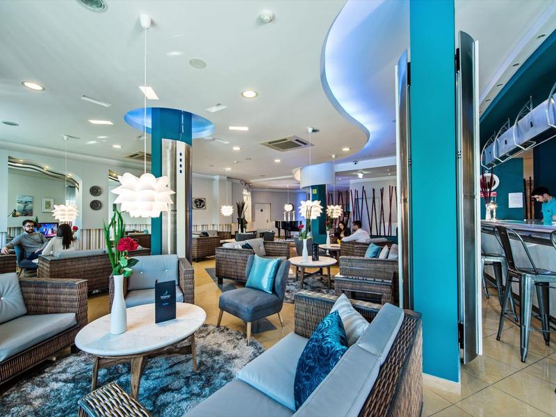 Modern eingerichteter Lounge-Bereich mit grauen Sofas, blauen Akzenten und beleuchtetem Barbereich.