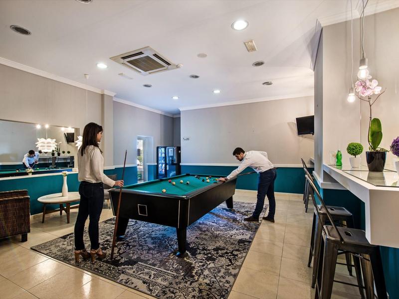 Moderne Spielzimmer mit Billardtisch, Teppich, Barbereich und zwei Personen, die Billard spielen.