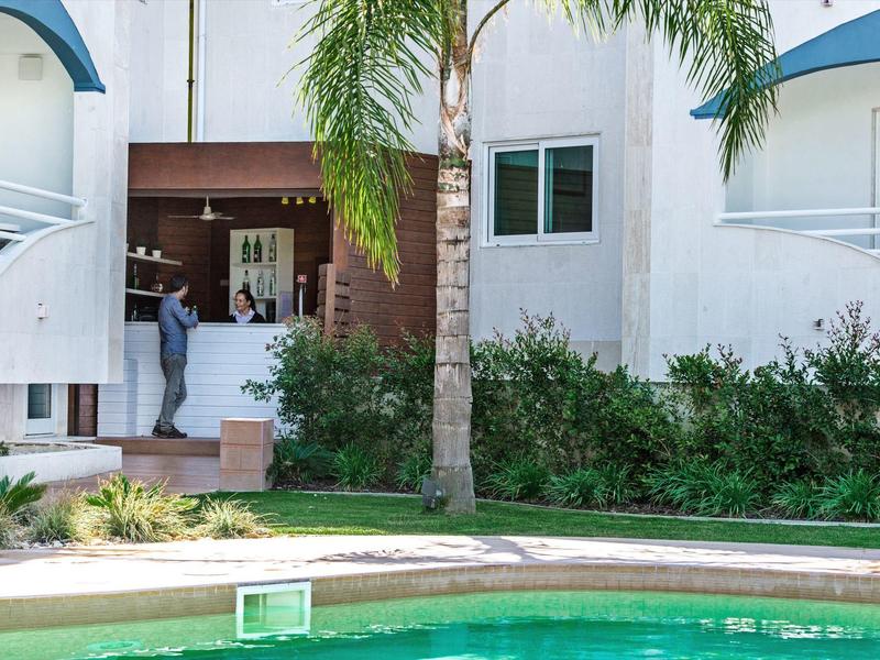 Moderner Hausgarten mit Pool, grünen Pflanzen und zwei Personen am Eingang unter Palmen.