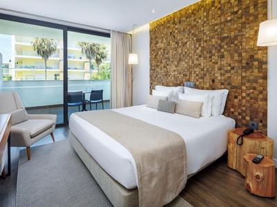 Modernes Hotelzimmer mit Doppelbett, Holzdekorwand und Balkon mit Stühlen.