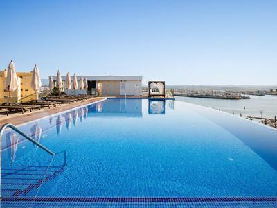 Infinity bazén s výhledem na moře a slunečné hotely pod čistou modrou oblohou.