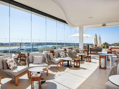 Terasa s pohodlnými pohovkami a stoly s výhledem na přístav za jasné oblohy.