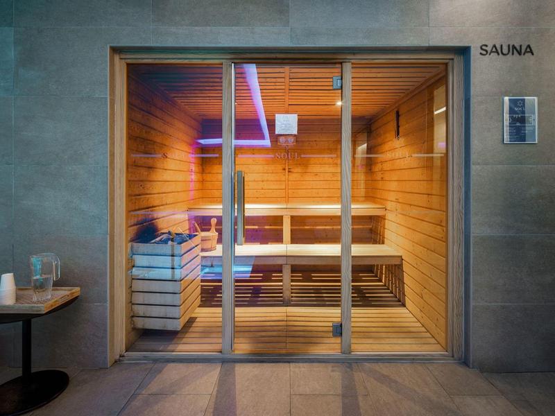 Pohled skrz prosklené posuvné dveře do moderní sauny s dřevěným obložením a lavicemi.