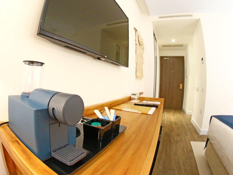 Hotelový pokoj s kávovarem na dřevěném stole a televizí na stěně.