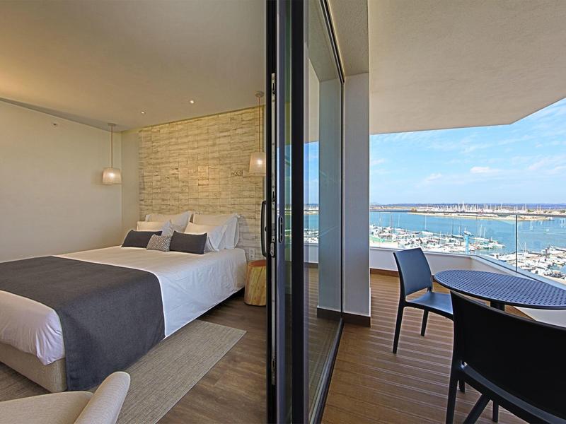 Moderní hotelový pokoj s výhledem na přístav z balkonu se stolem a židlemi.
